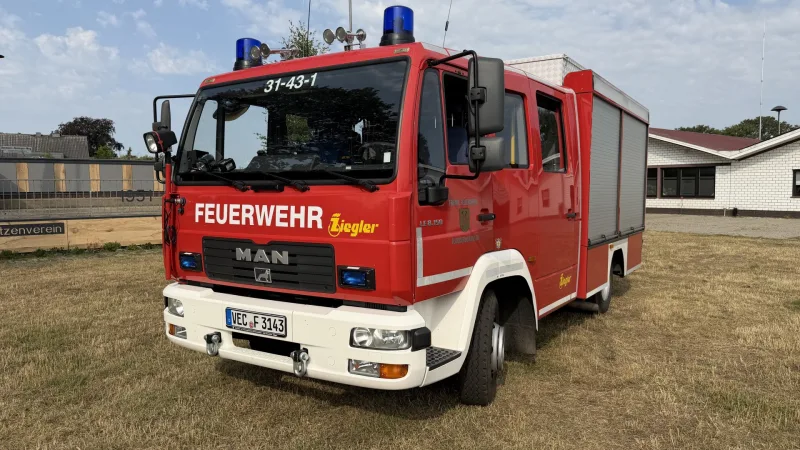 Das LF 8 schräg von vorn auf der Wiese, mit Blaulichtern und dem Funkrufnamen 31-43-1 an der Frontscheibe.