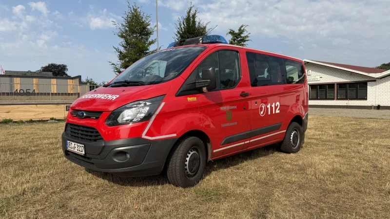 Mannschaftstransportfahrzeug der Feuerwehr Fladderlohausen schräg von vorn, das Schützenhaus im Hintergrund.