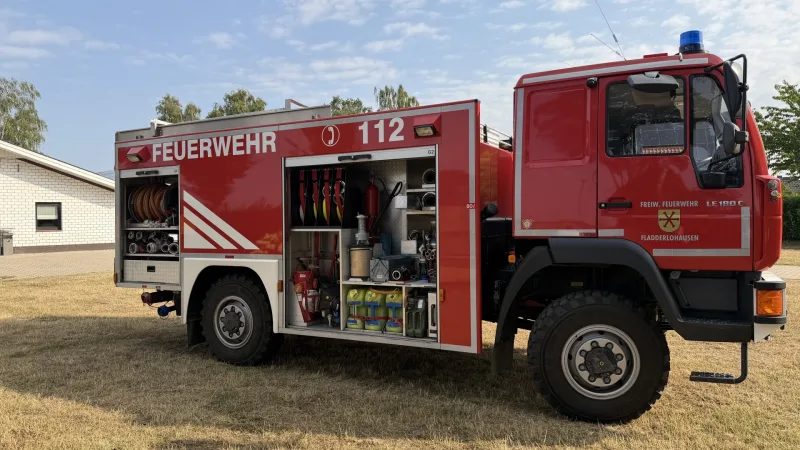Beifahrerseite des TLF 16/24 Tr mit geöffneten Geräteräumen: Strahlrohre, ein Feuerlöscher und Kanister in den Regalen.