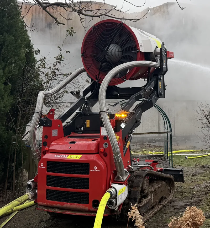TAF 35 im Einsatz: rotes Raupenfahrzeug mit großer Turbine, die Wassernebel ausstößt, angeschlossen an gelbe Schläuche.