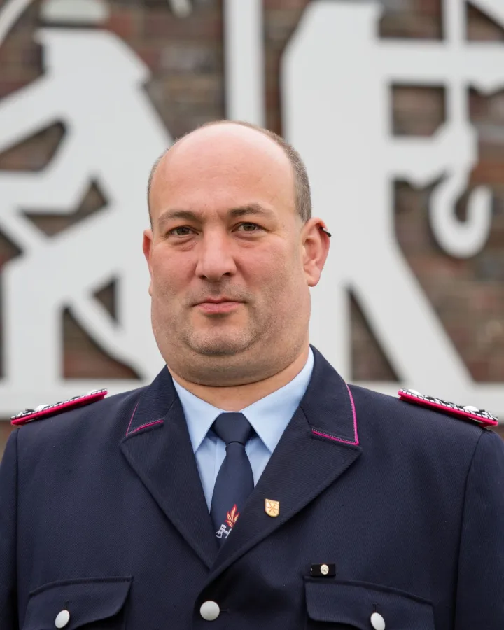 Porträt von Mathias Lüpke-Narberhaus in dunkelblauer Uniform vor einer Klinkerwand.