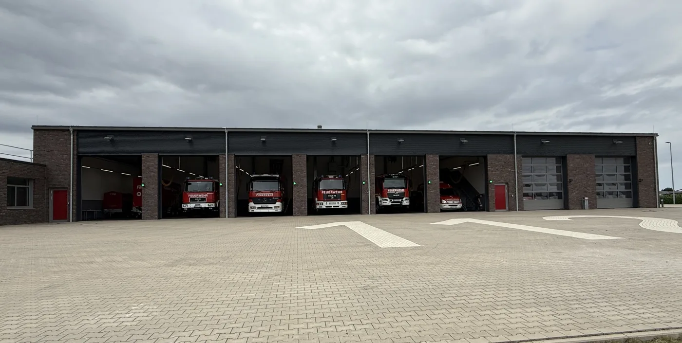 Die Fahrzeughalle des Feuerwehrhauses Holdorf mit acht Toren nebeneinander; in den sechs offenen Toren stehen die Einsatzfahrzeuge, die beiden rechten Tore sind geschlossen.