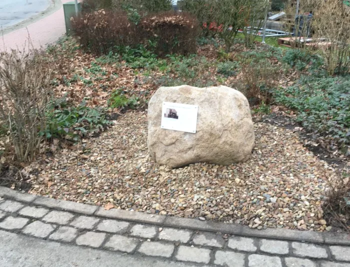Ein großer Findling mit einer kleinen Tafel in einem Beet an der evangelischen Kirche.