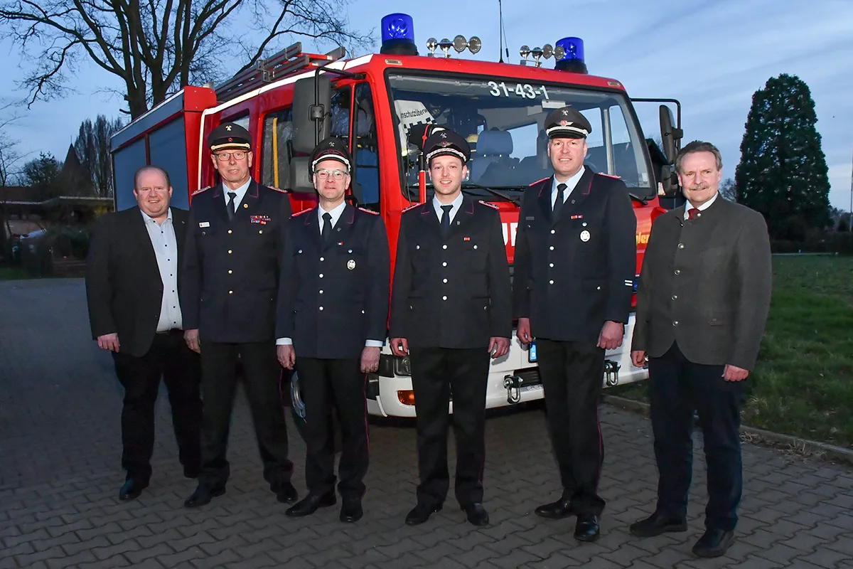 Sechs Männer, vier davon in Dienstuniform der Feuerwehr, stehen in der Abenddämmerung vor dem Löschfahrzeug mit dem Funkrufnamen 31-43-1.