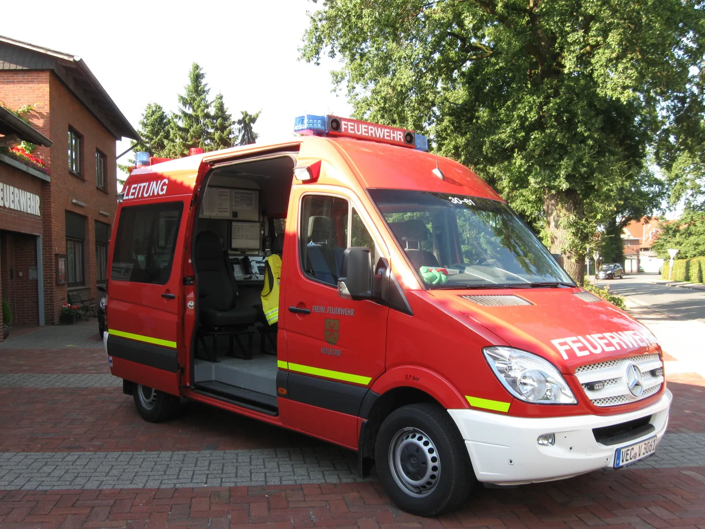 Roter Mercedes Sprinter mit der Aufschrift Leitung und geöffneter Schiebetür, innen ein Arbeitsplatz mit Bildschirmen.