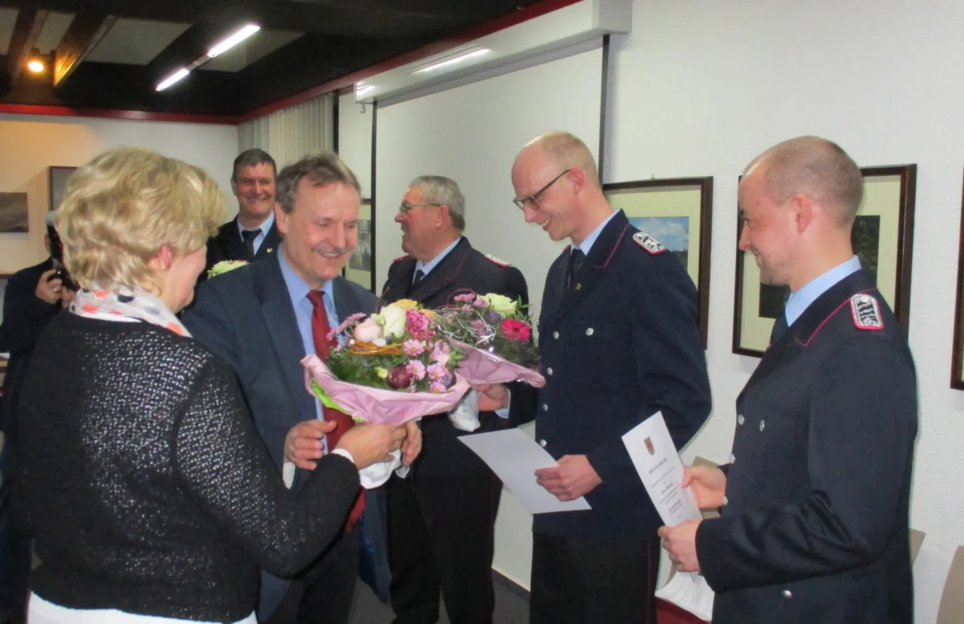 In einem Sitzungsraum werden Blumensträuße und Urkunden an Führungskräfte der Feuerwehr in Dienstuniform überreicht.