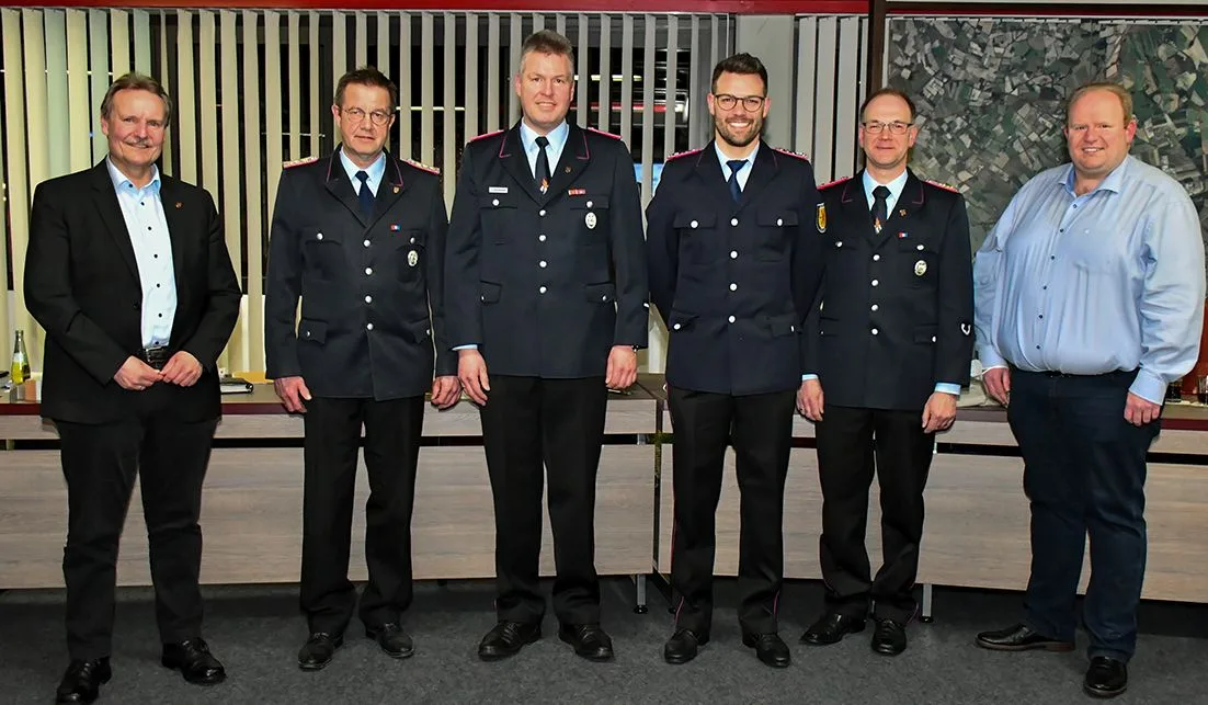 Sechs Männer stehen nebeneinander in einem Sitzungssaal, vier davon in Dienstuniform der Feuerwehr.