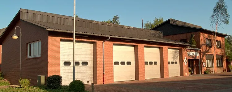 Feuerwehrhaus aus Klinker mit vier weißen Sektionaltoren, rechts das zweigeschossige Gebäude mit dem Schriftzug Feuerwehr.