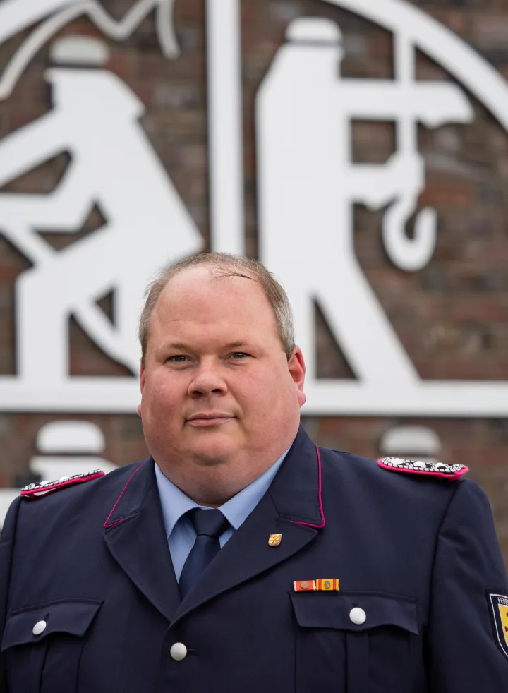 Porträt von Jens Lindemann in dunkelblauer Uniform vor einer Klinkerwand.
