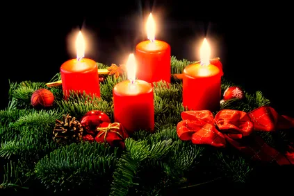 Adventskranz aus Tannengrün mit vier brennenden roten Kerzen, Zapfen und roten Schleifen.